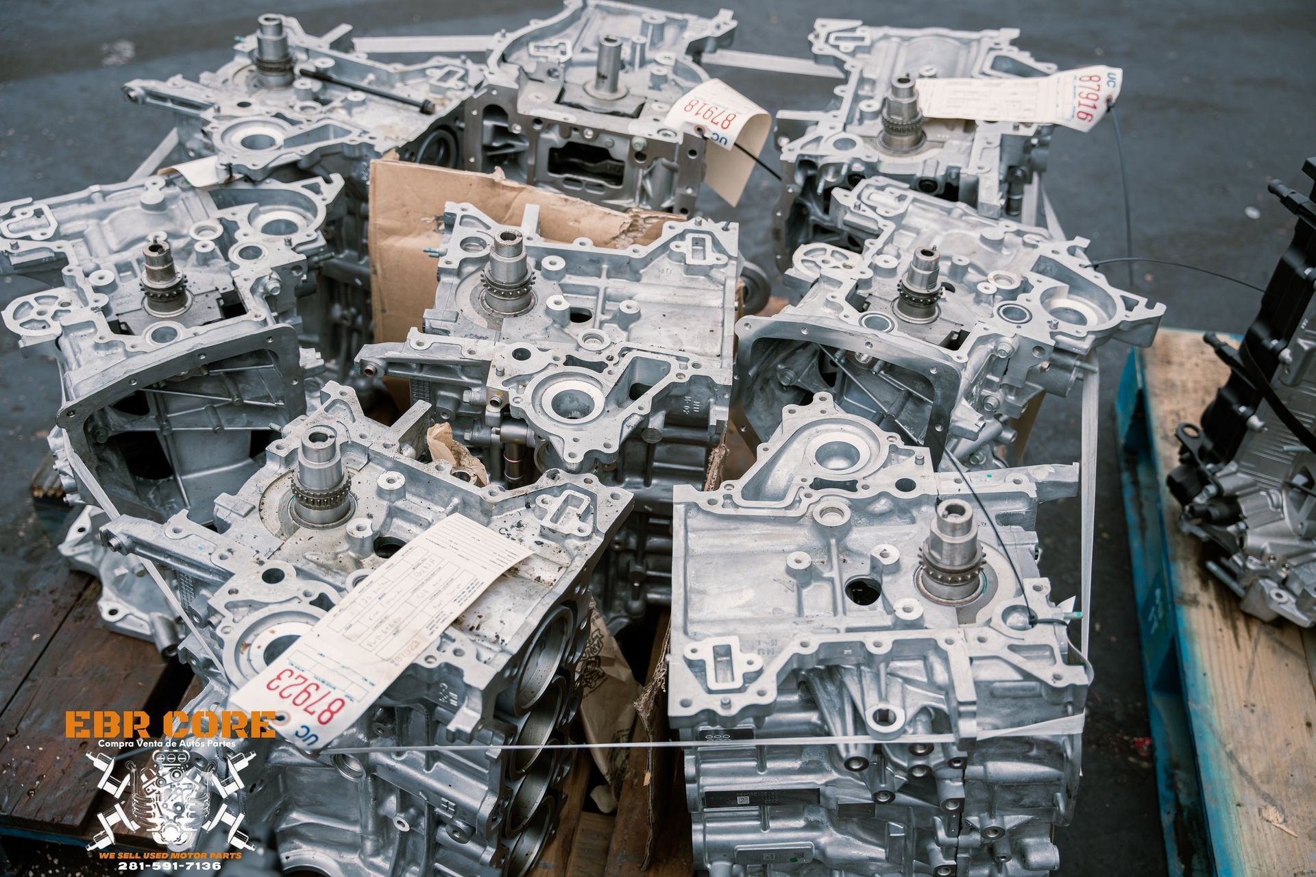 A pile of silver engine blocks at a factory, with some cardboard and paperwork.
