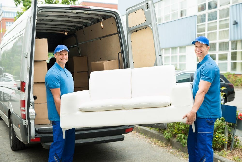 Two Men Are Carrying A White Couch Out Of A Van — Greater Newcastle Removals In Gwandalan, NSW