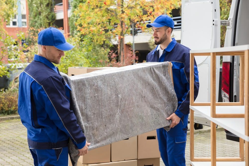 Two Movers Are Carrying A Couch In Front Of A Van — Greater Newcastle Removals In Charlestown, NSW