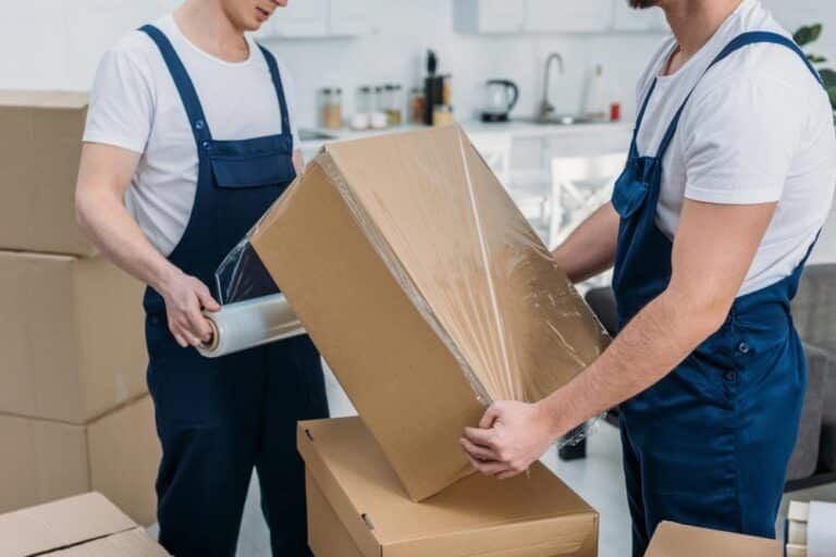 Two Men Are Wrapping A Cardboard Box With Plastic Wrap — Greater Newcastle Removals In Rathmines, NSW