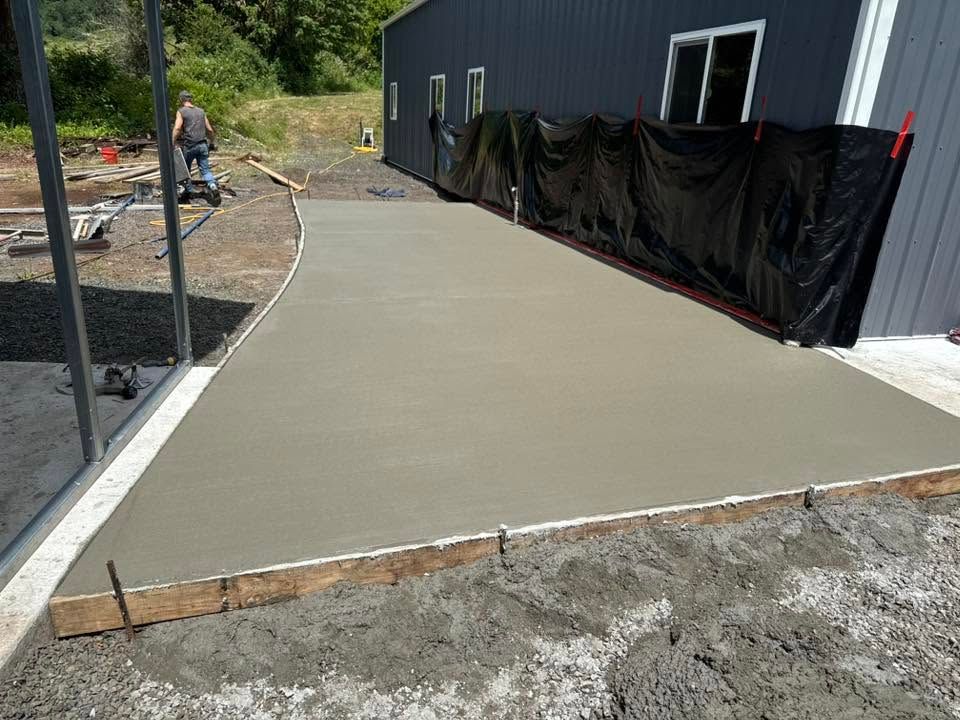 Fresh concrete driveway slab beside a black building under construction