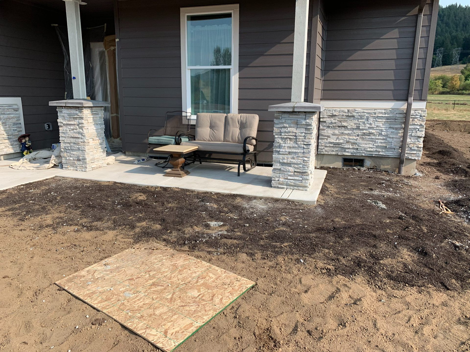 House porch with stone columns, patio chairs, and bare dirt landscaping under construction