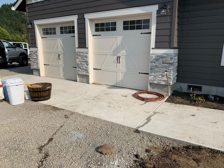 Two-car garage with white doors, stone trim, and a driveway with buckets and a basket.