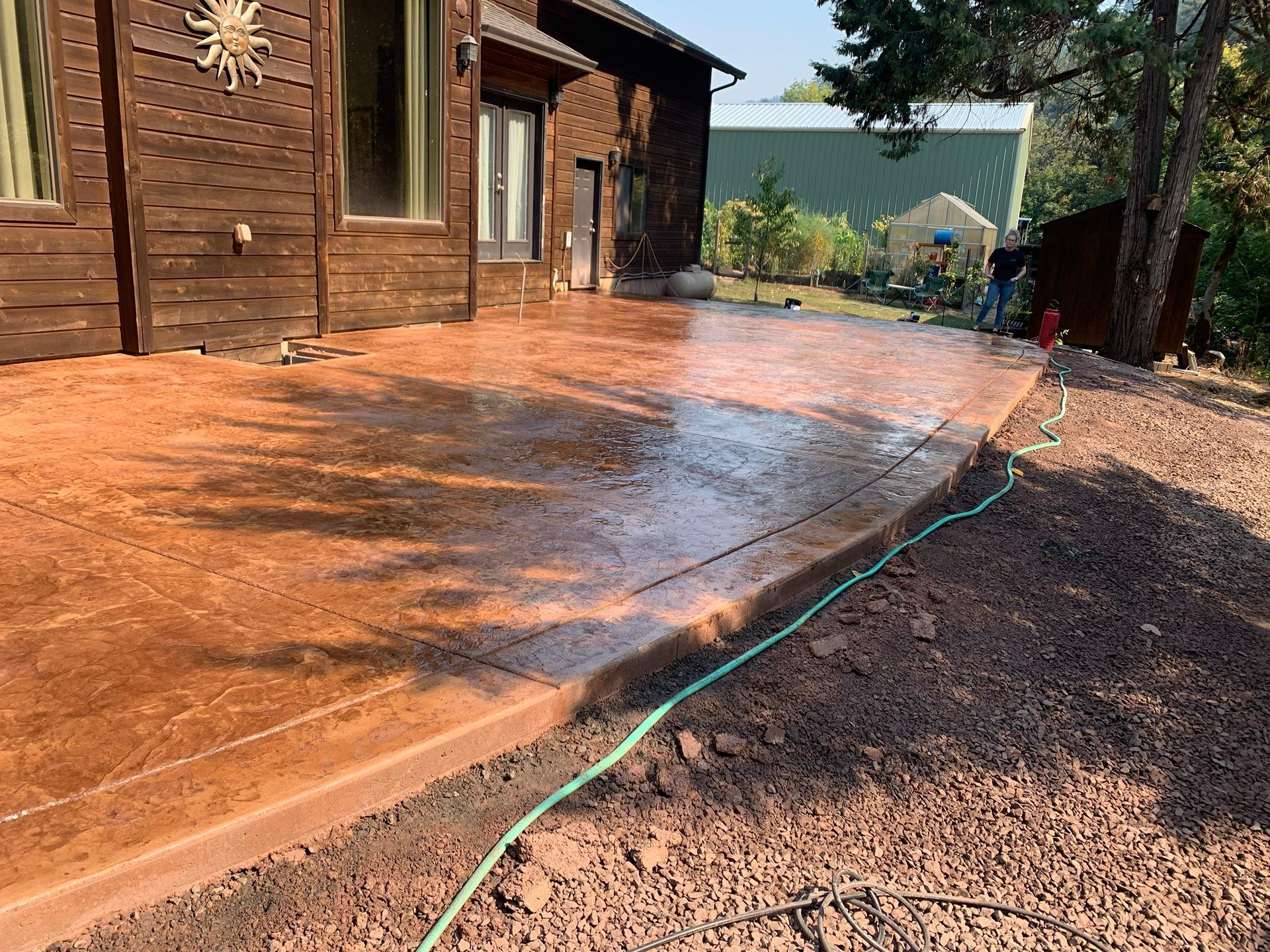 Wooden deck being rinsed with a hose beside a log house on a sunny day