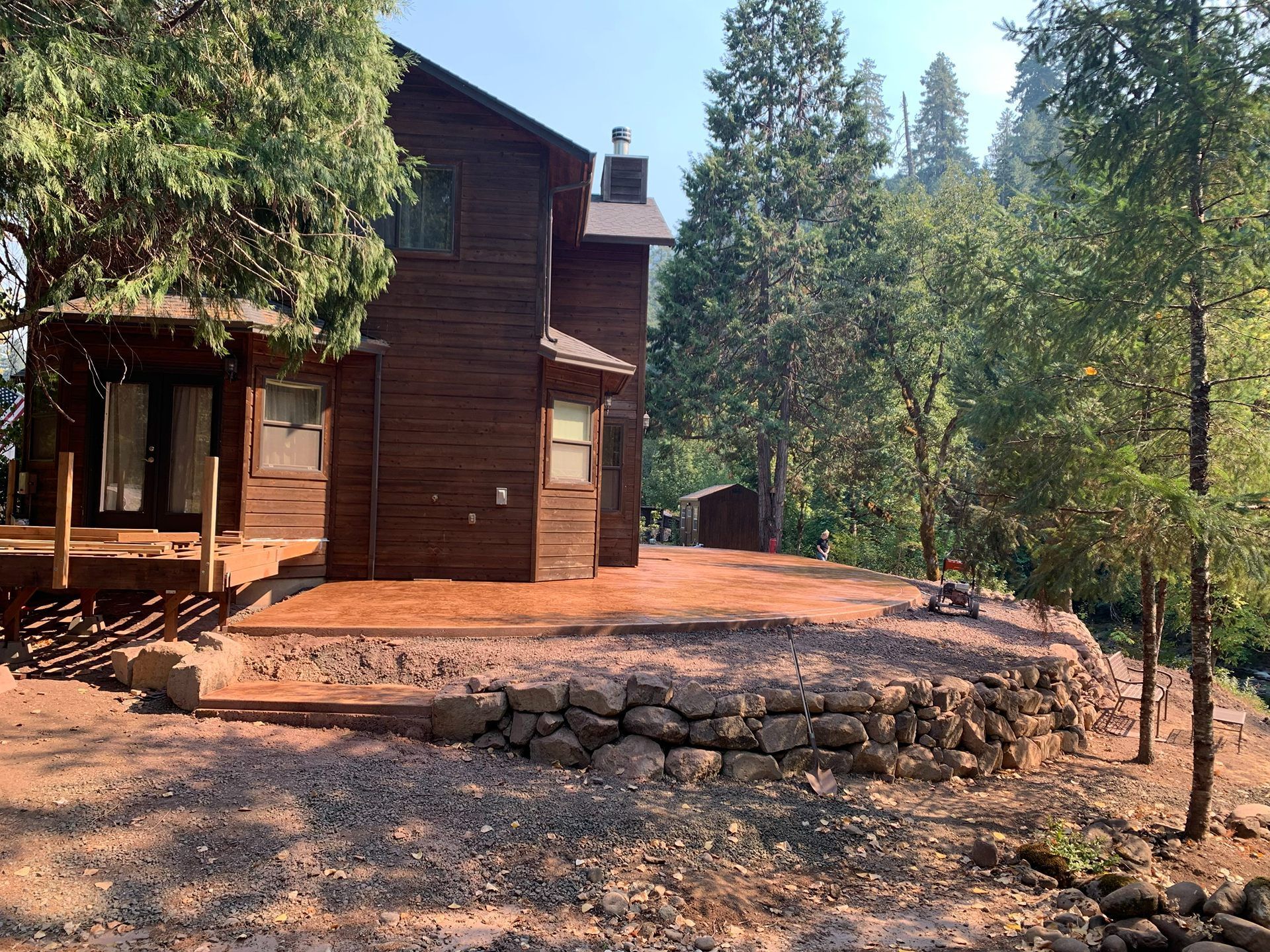 Rustic wooden cabin beside a stone terrace in a sunlit pine forest