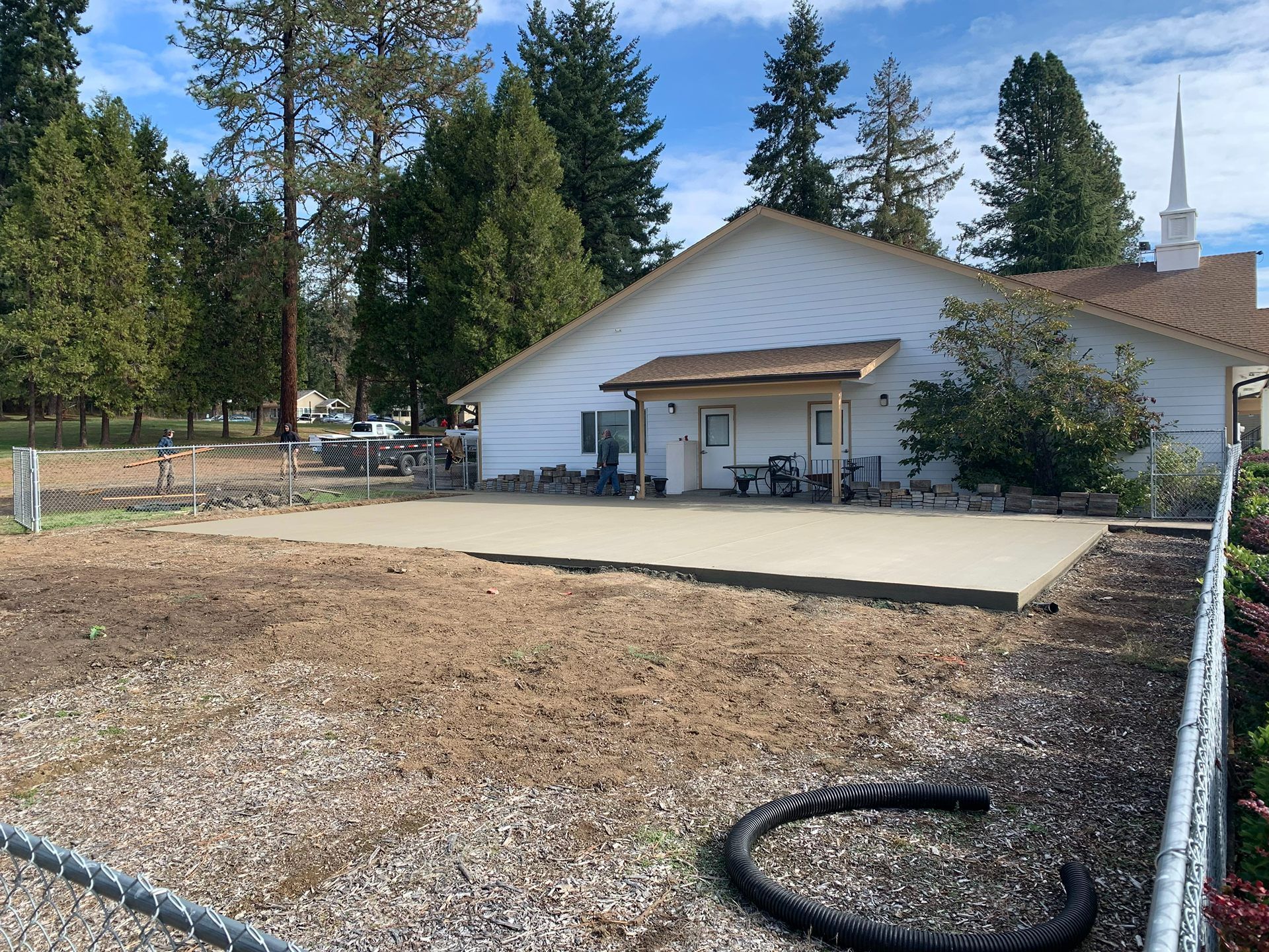 Rural house with a large concrete patio, gravel yard, and pine trees in the background