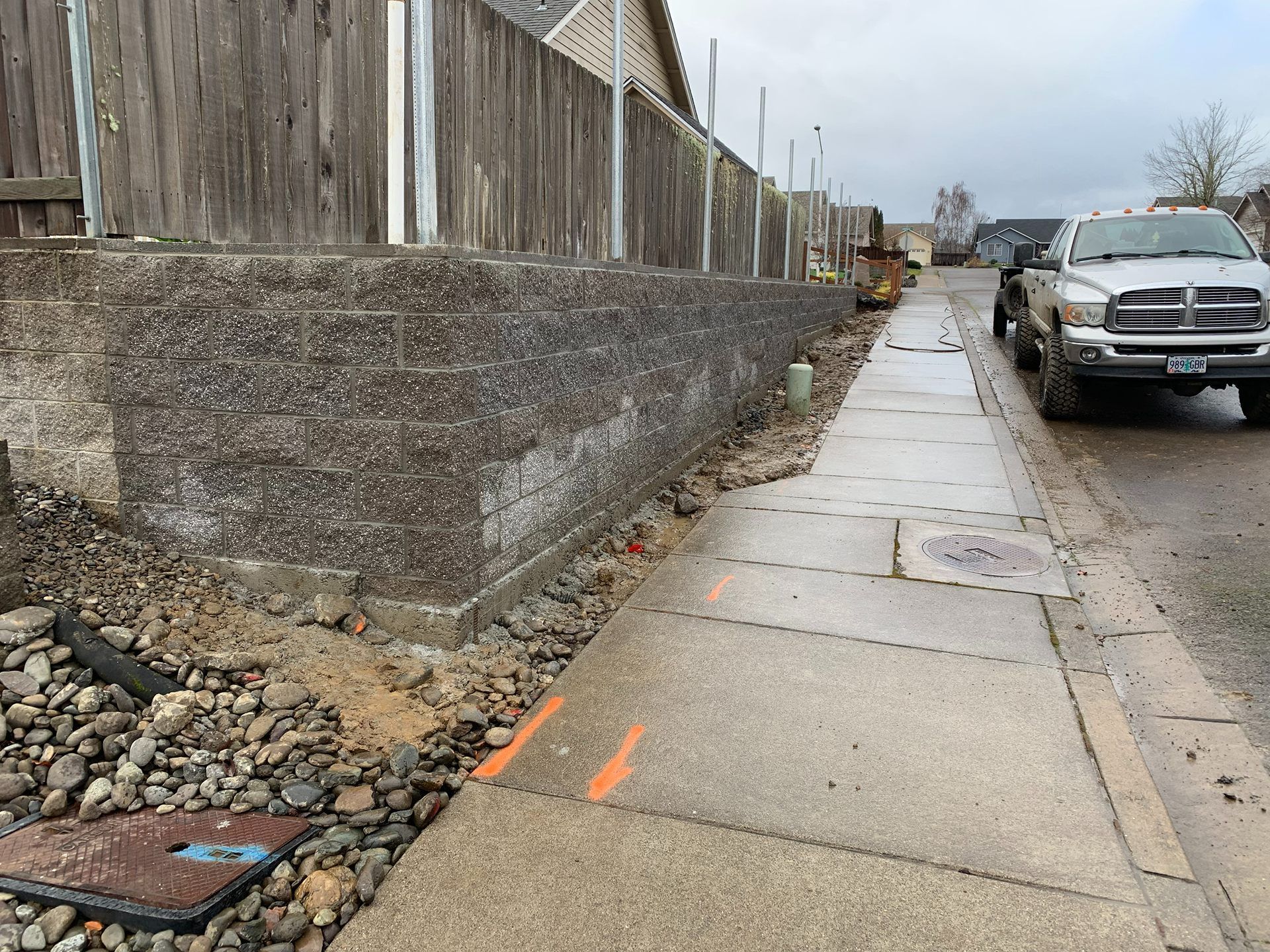 Broken sidewalk beside a retaining wall and parked pickup trucks on a wet street.