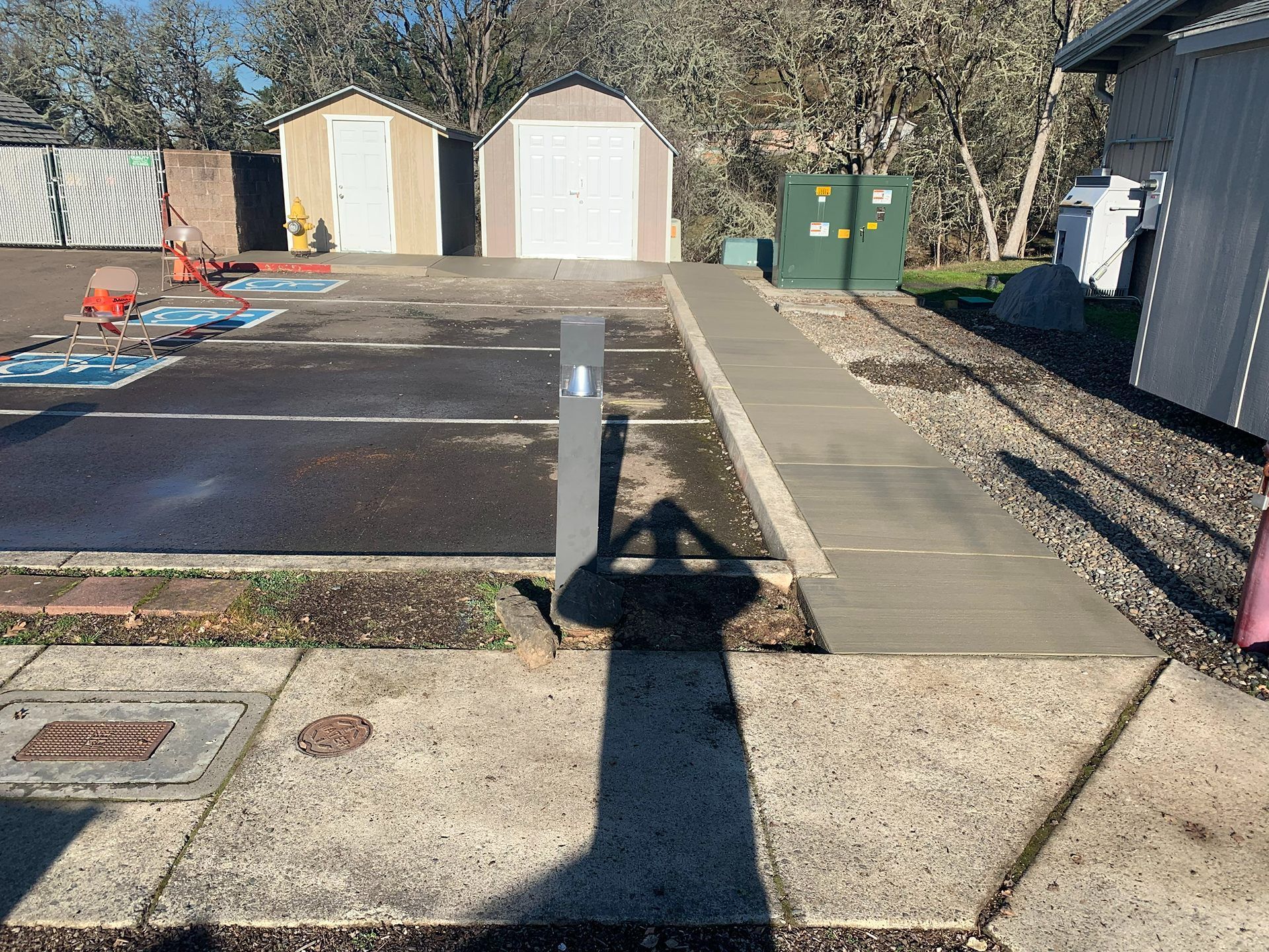Empty parking lot with two white sheds, green bins, and a shadow of the photographer in the foreground.
