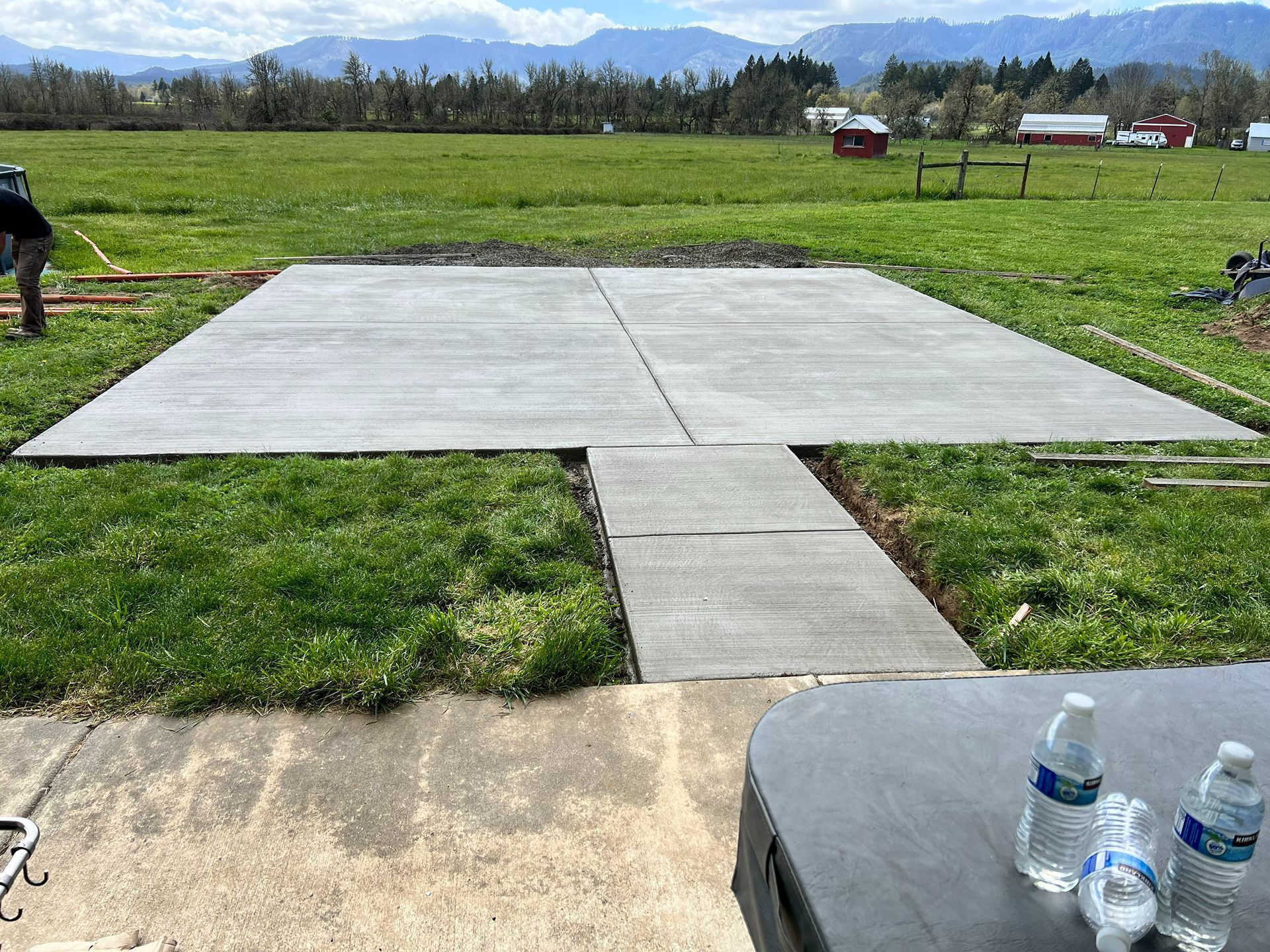Concrete slab in grassy field with mountains in the distance and water bottles on a table in the foreground