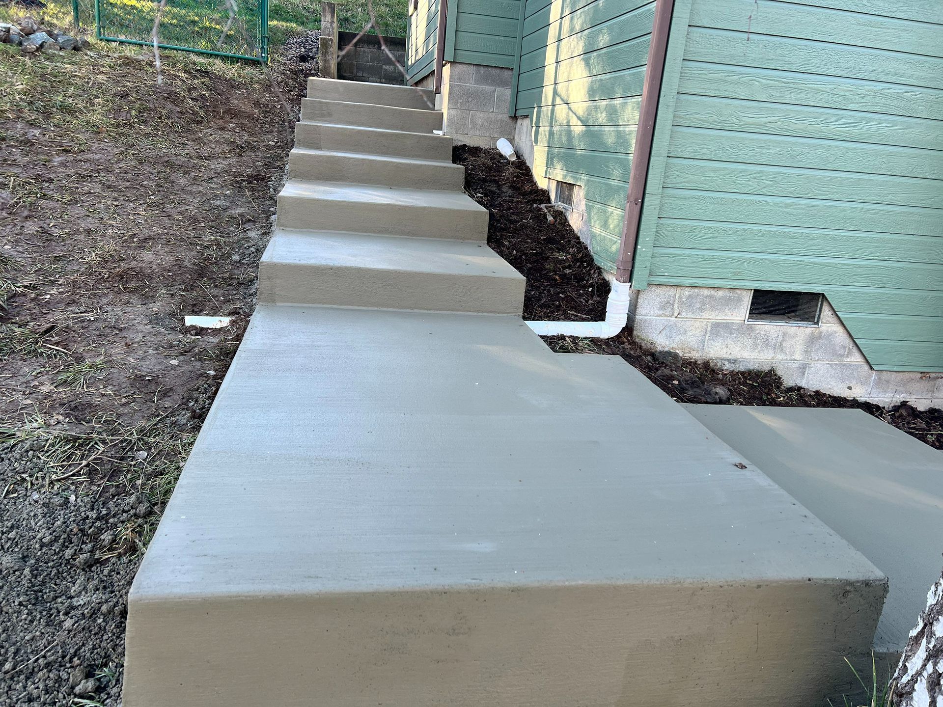 Concrete accessibility ramp with steps beside a green brick building and dirt slope