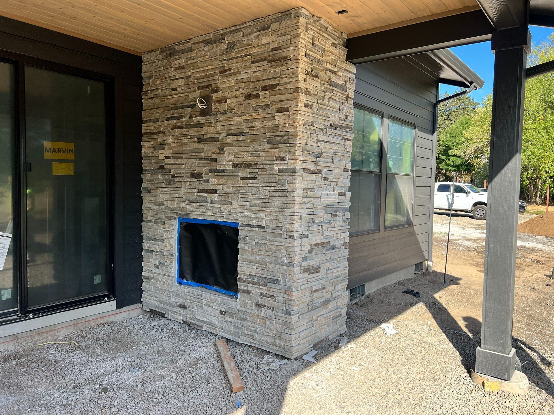 Stone exterior wall with a small blue-taped opening under a covered porch.