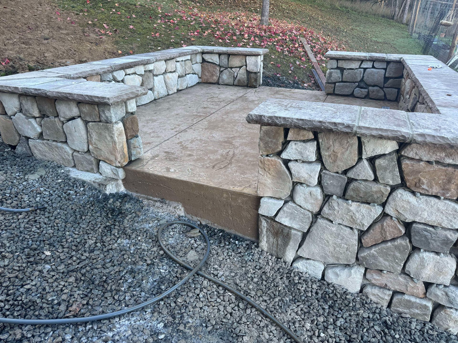 Stone patio with built-in curved seating walls and a concrete center area in an outdoor yard.