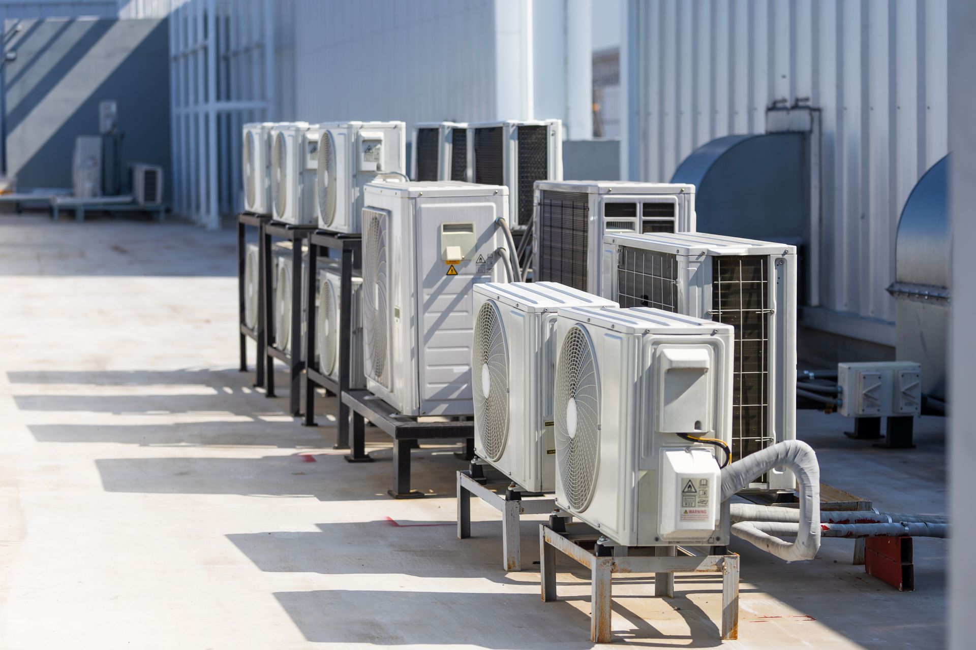 Outdoor row of HVAC units on metal stands beside a building