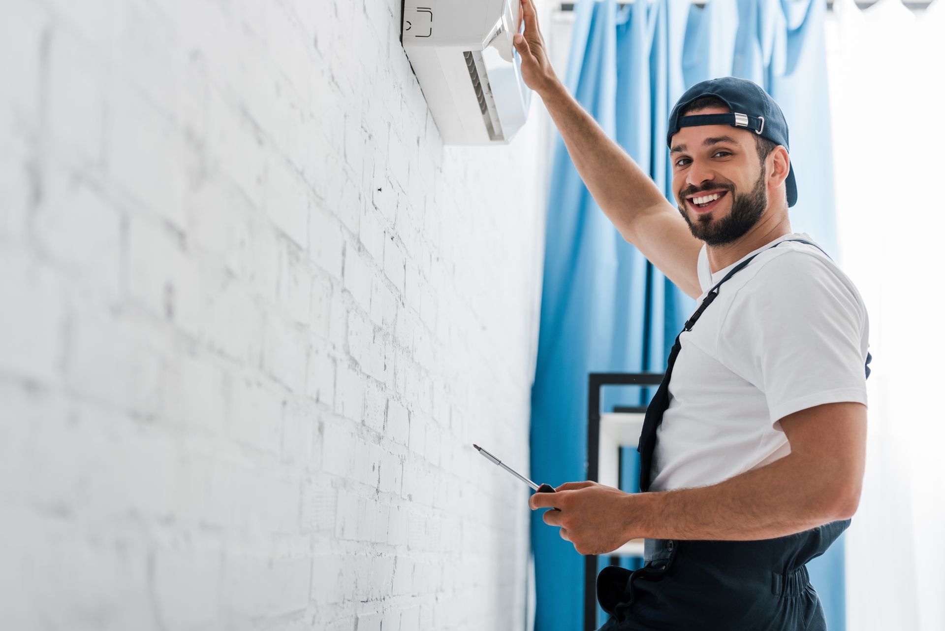 Smiling workman looking at camera while repairing air conditioner.