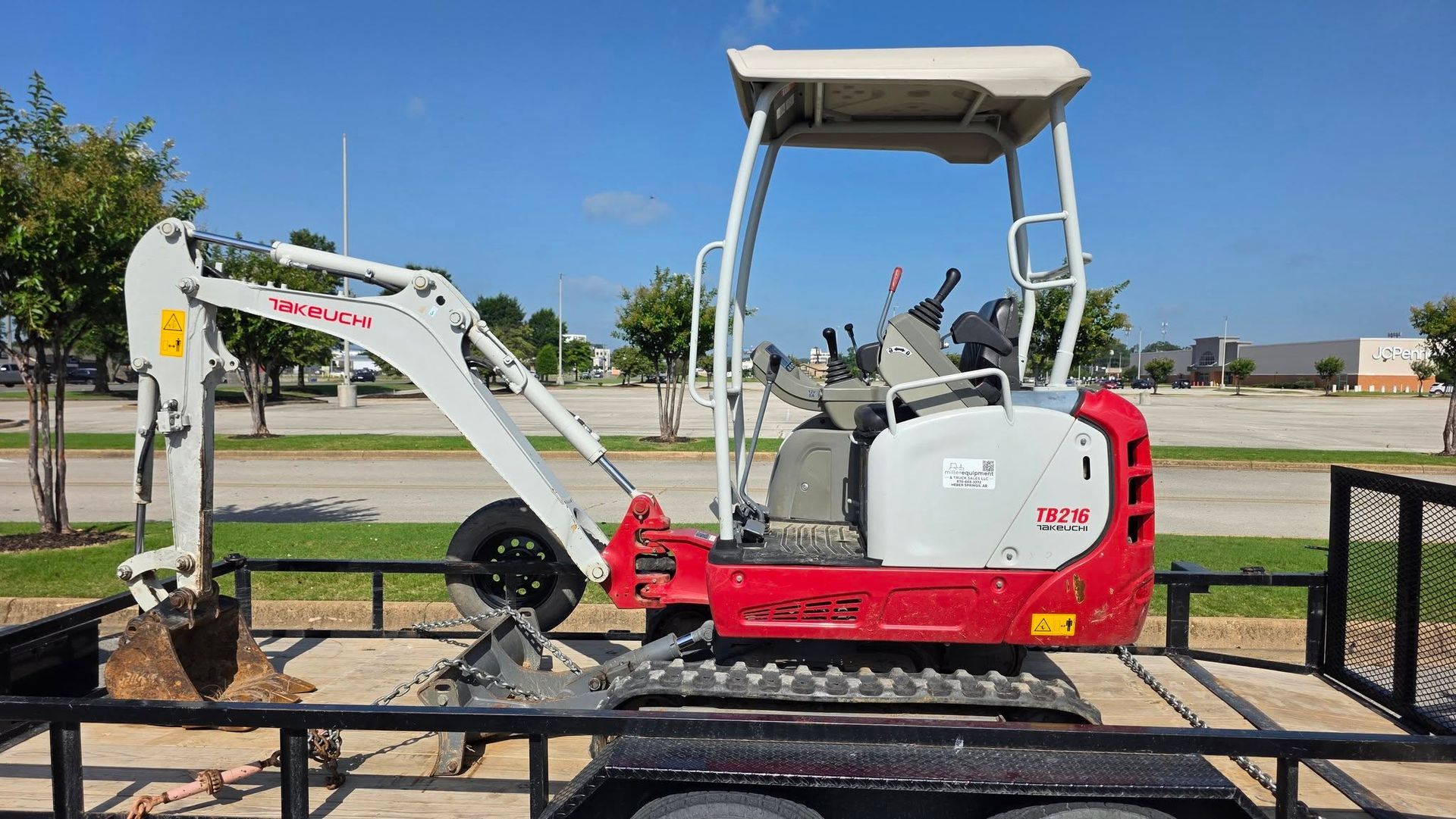 Red mini excavator on a trailer at a construction yard under a clear sky