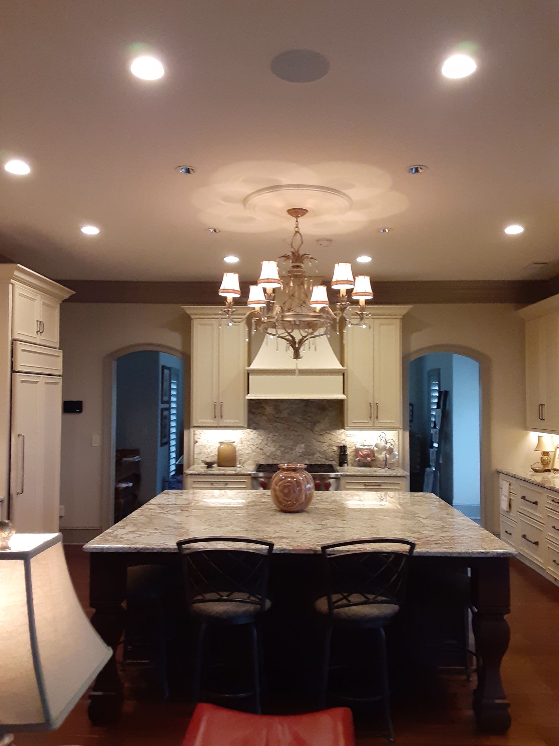 Spacious kitchen with a large marble island, cream cabinets, chandelier, and recessed ceiling lights.