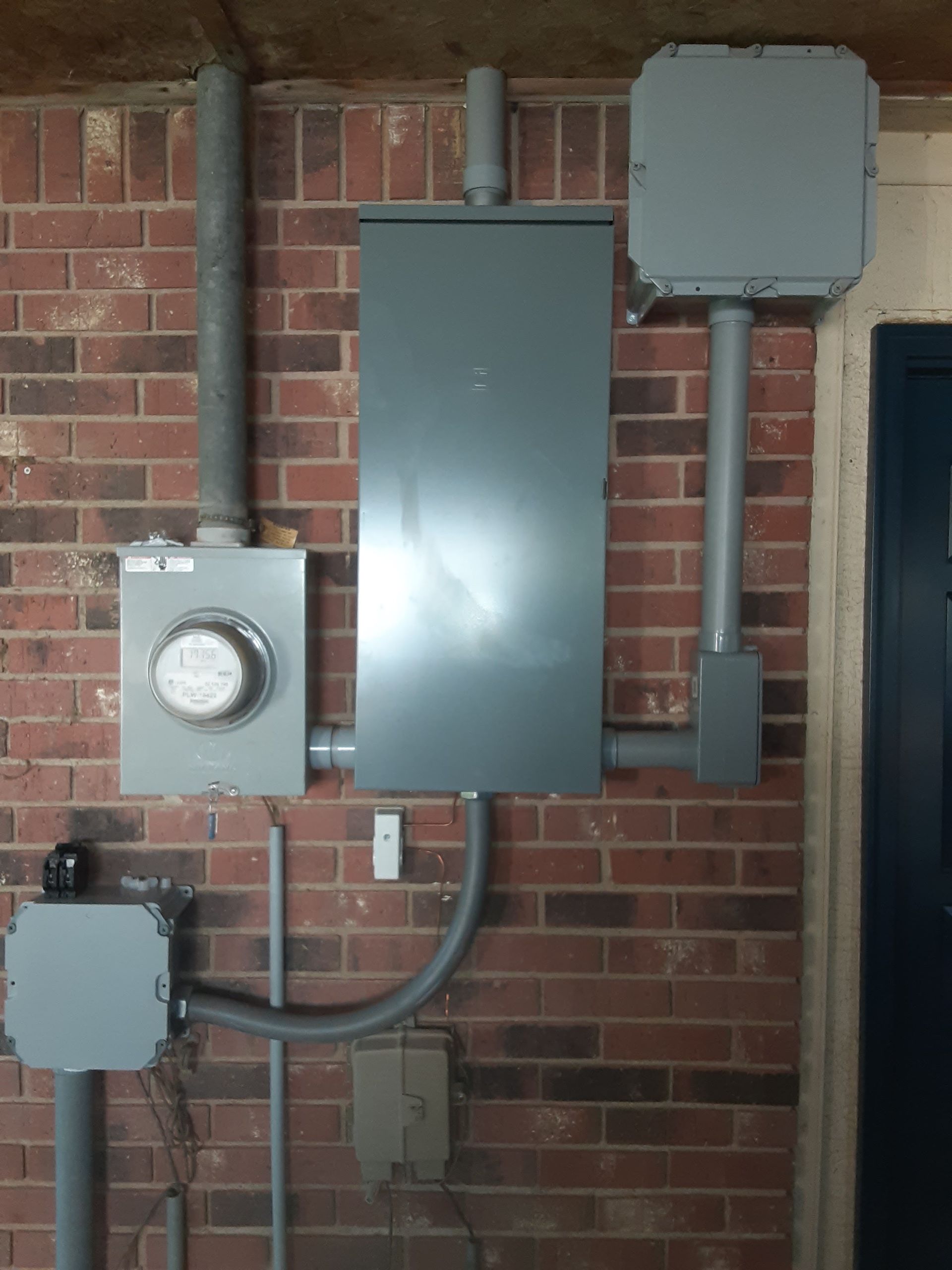 Gray electrical service boxes and meter mounted on a brick wall with conduit piping