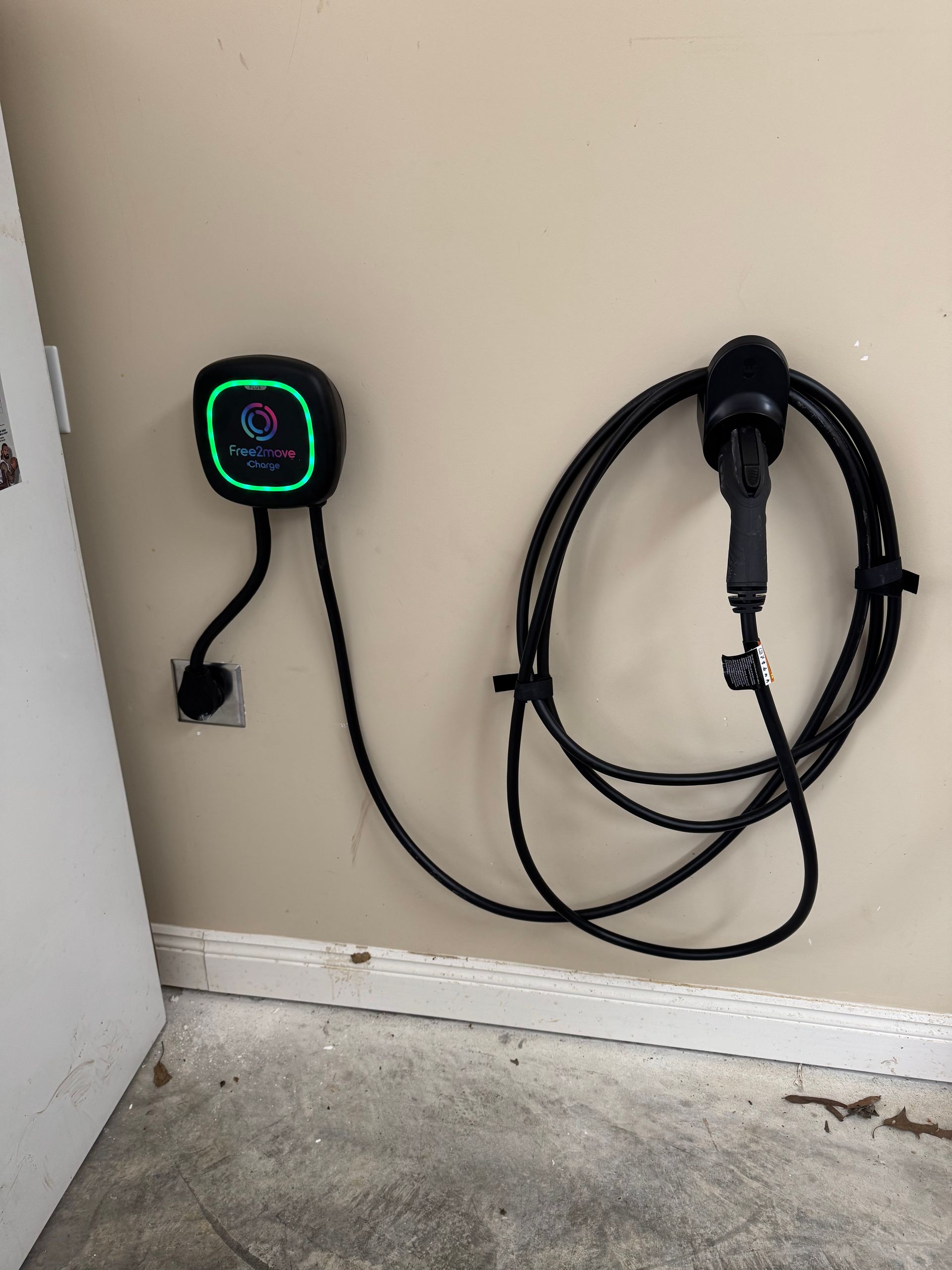 Wall-mounted EV charger with coiled cable beside a garage door on a concrete floor