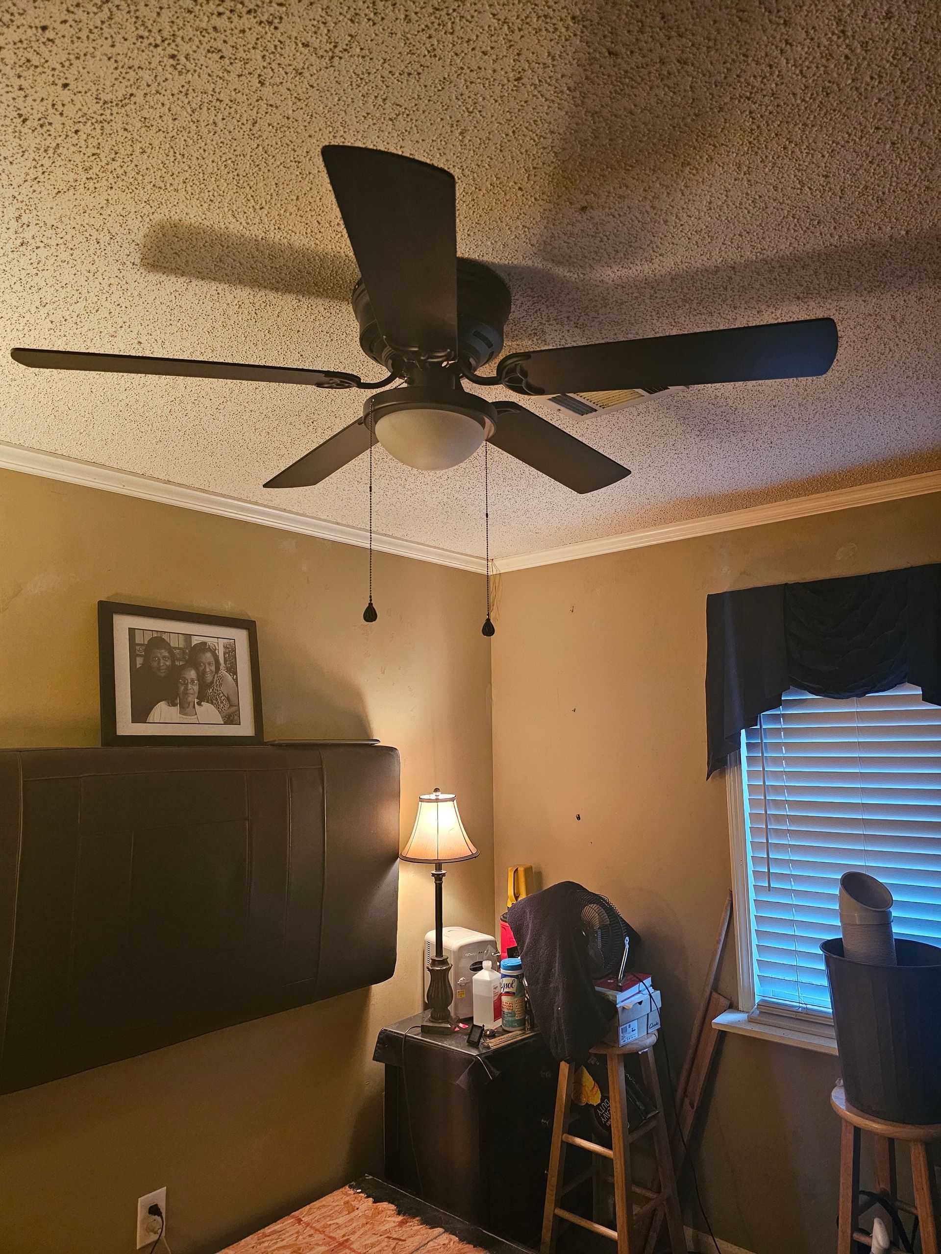 Bedroom with ceiling fan, wall-mounted TV, lamp, desk, and window with blinds.