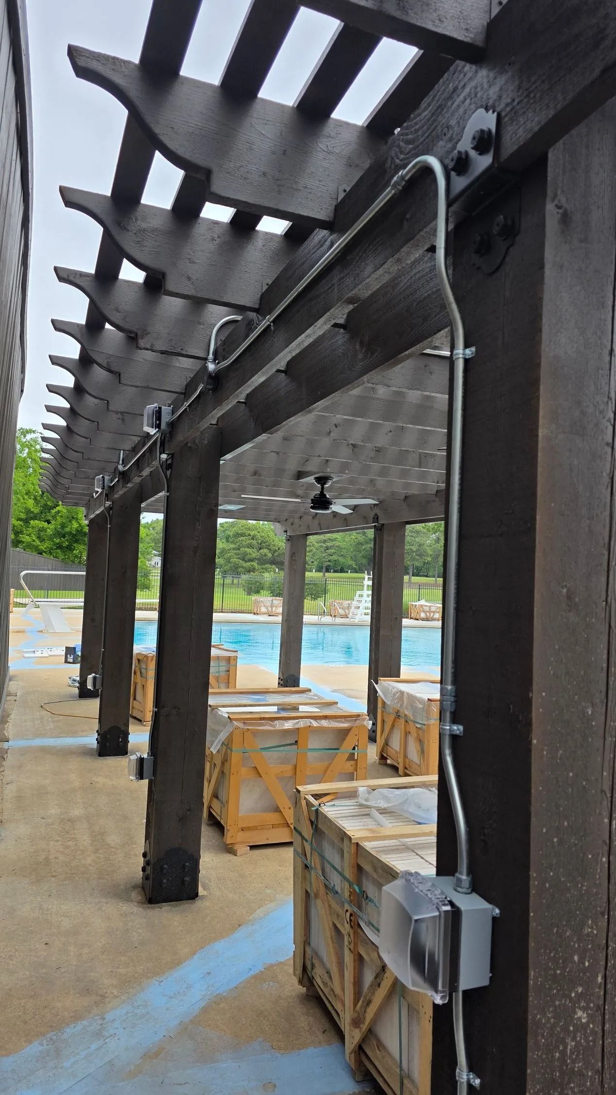 Covered outdoor walkway with dark posts and beams beside stacked wooden crates and a blue-painted floor