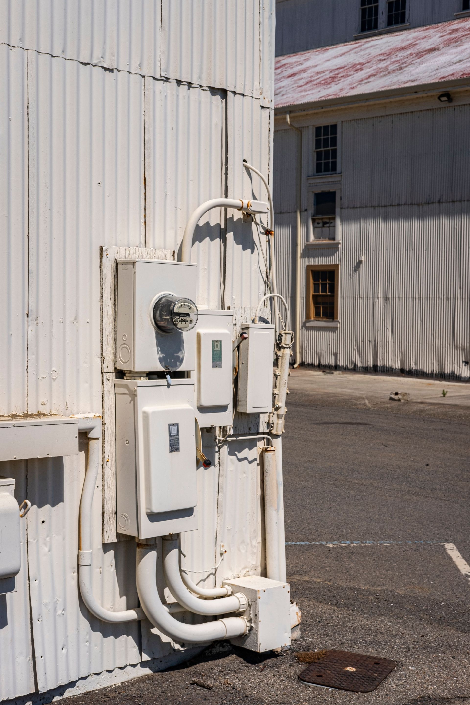 White utility boxes and pipes mounted on a corrugated metal wall beside an alleyway