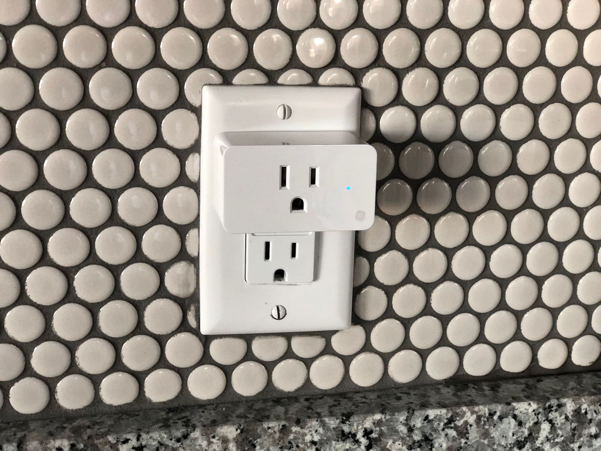 White wall outlet on a small black-and-white circular tile backsplash.