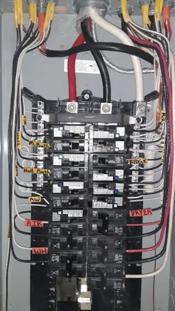 Electrical breaker panel with multiple labeled breakers and colored wires connected inside.