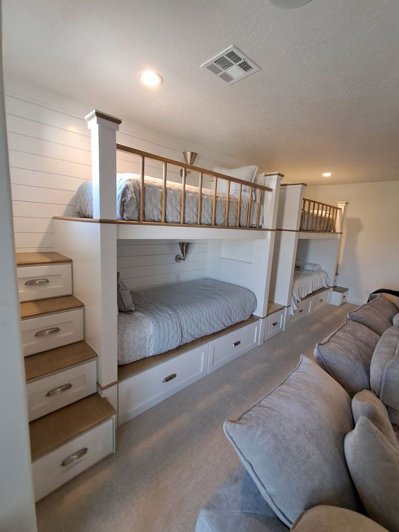 Built-in bunk beds with stairs, white and wood. Two beds visible. Light-colored rug and wall.
