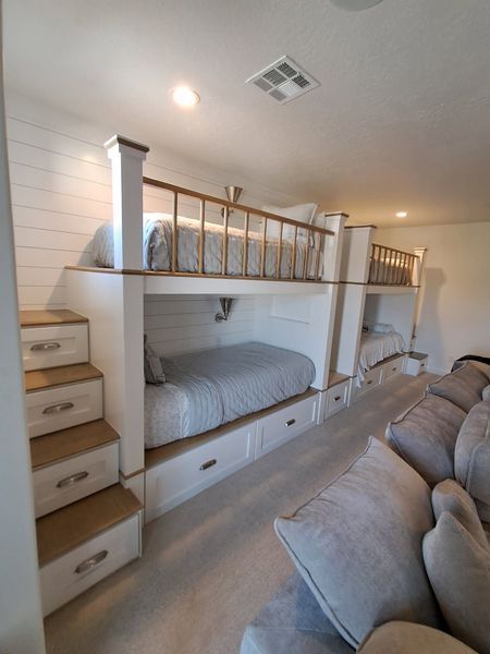 Built-in bunk beds with stairs and drawers, in a light-colored room, next to a gray sofa.