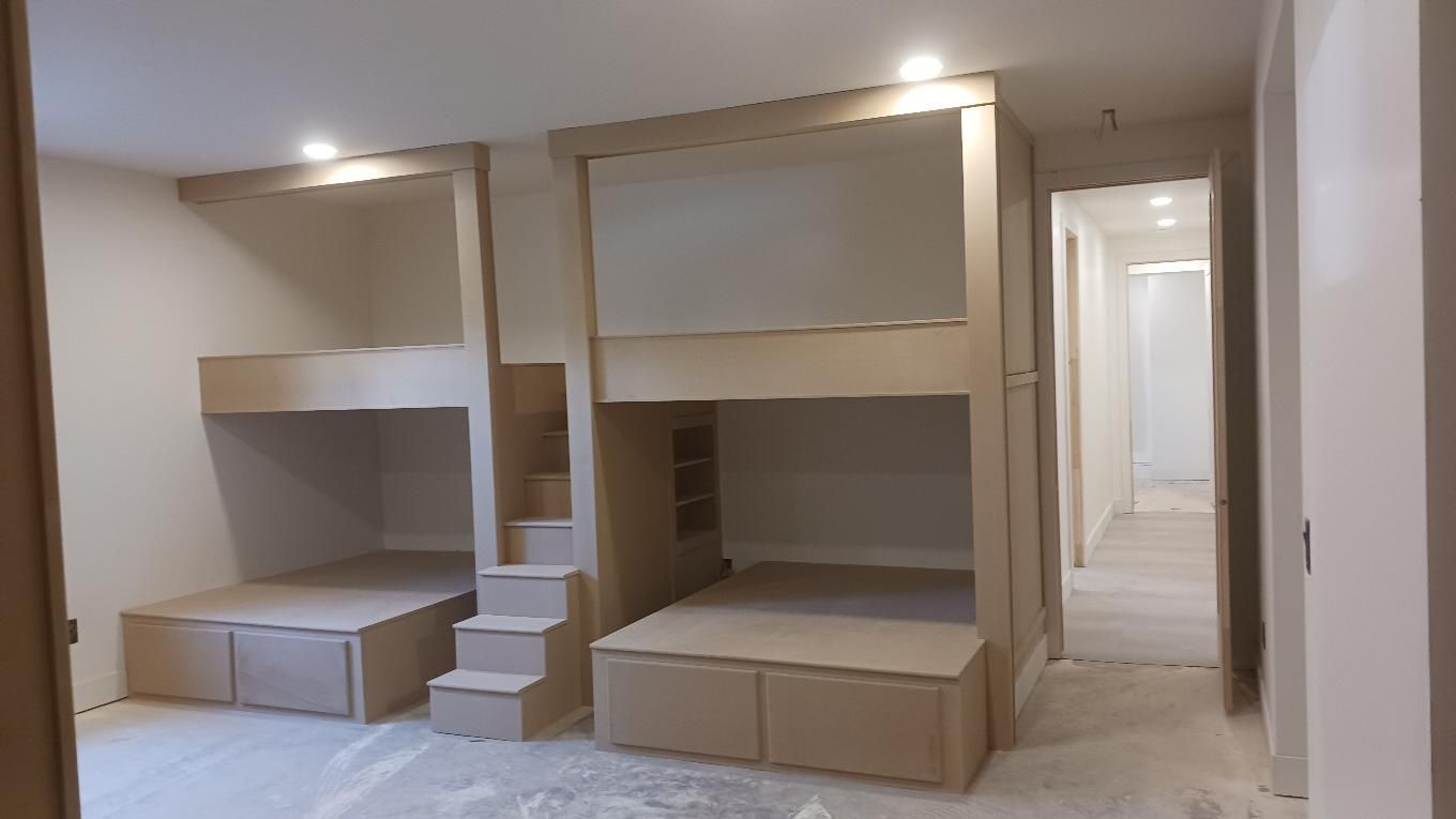 Two built-in bunk beds with stairs and storage drawers in a light-colored room.