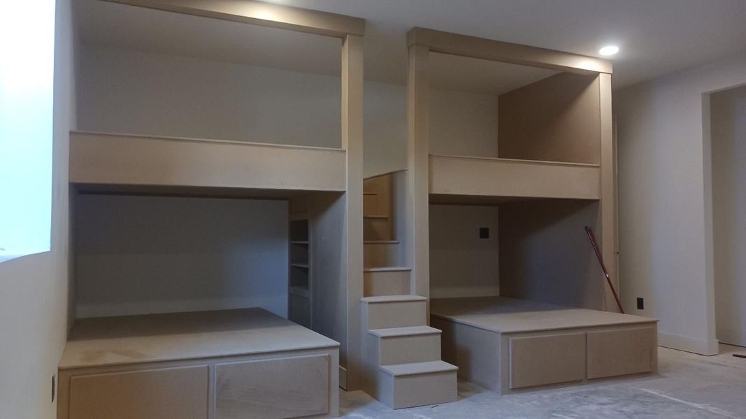 Two custom-built bunk beds with stairs in a room. Wooden frames, with lower storage cabinets.