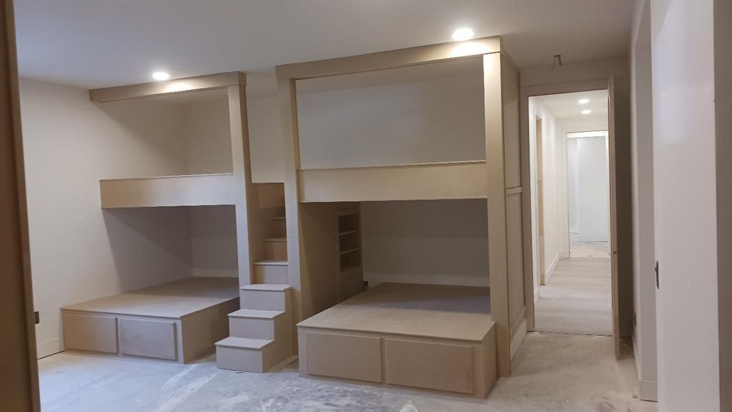 Built-in bunk beds in a room. Light wood finish, stairs lead to top bunk. Light fixtures recessed in ceiling.