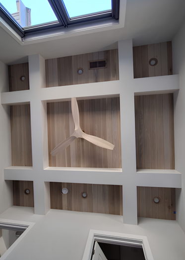 Wooden ceiling with a fan and recessed lights, under a skylight.