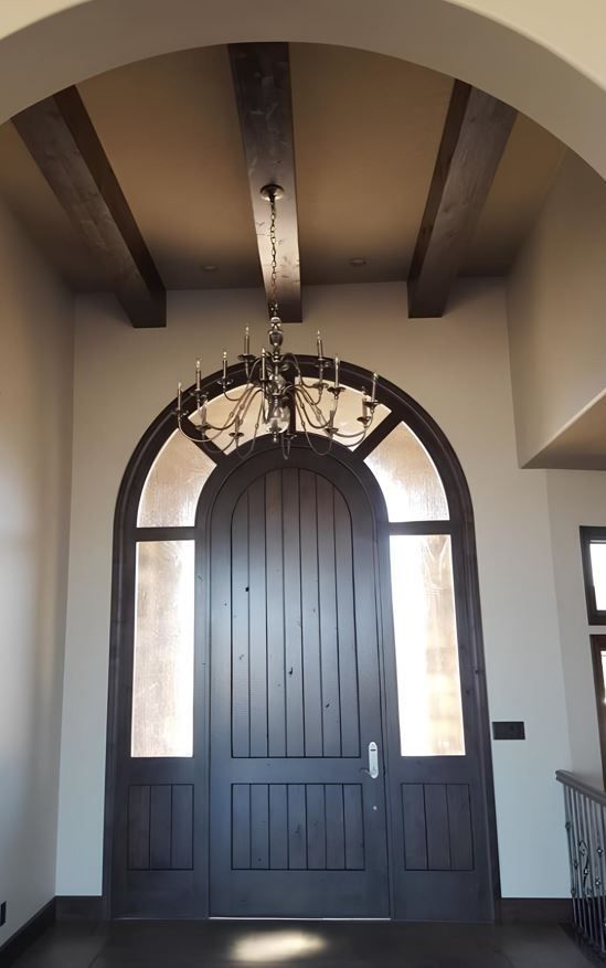 Arched black front door beneath exposed wooden beams in a bright entryway