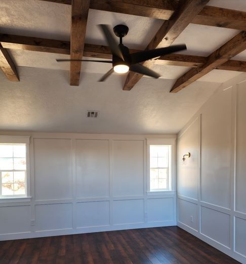 Bedroom with dark wood floor, white paneled walls, wooden ceiling beams, and a black ceiling fan.