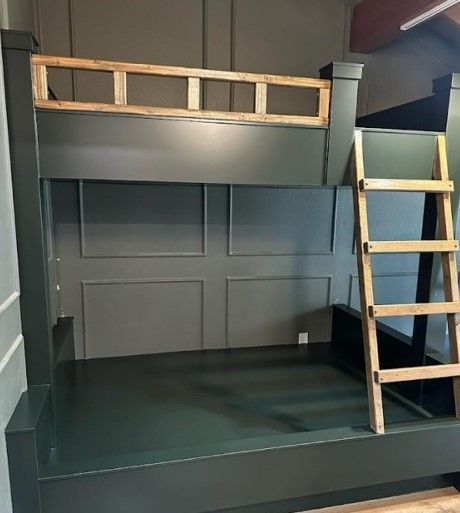 Dark green bunk bed with wooden ladder and light-colored wood detailing on the upper bunk.