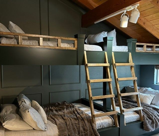 Dark green bunk beds with wooden ladders and trim, pillows, and blankets.
