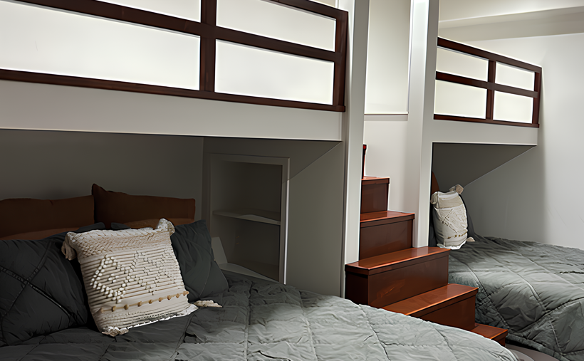 Two bunk beds in a white room, with dark wood accents, gray bedding, and a small set of stairs.