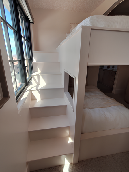 White bunk bed with built-in stairs next to a window. Sunlight streams in.