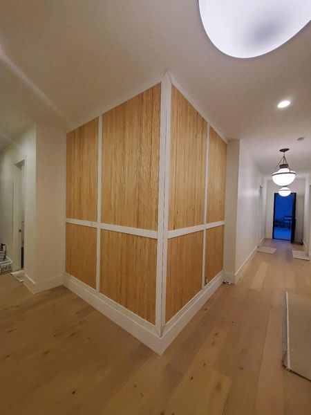 Hallway with wood-paneled corner wall, light wood floors, white trim, and ceiling lights leading to a blue doorway.