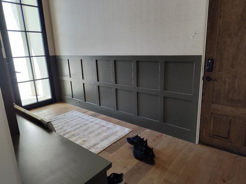 Entryway with dark green wainscoting, light rug, wood door, and a side table.