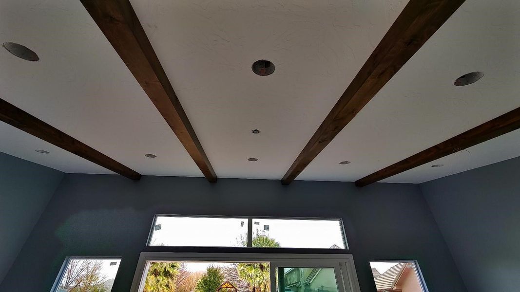 Gray walls with windows, white ceiling with wooden beams and recessed lights.