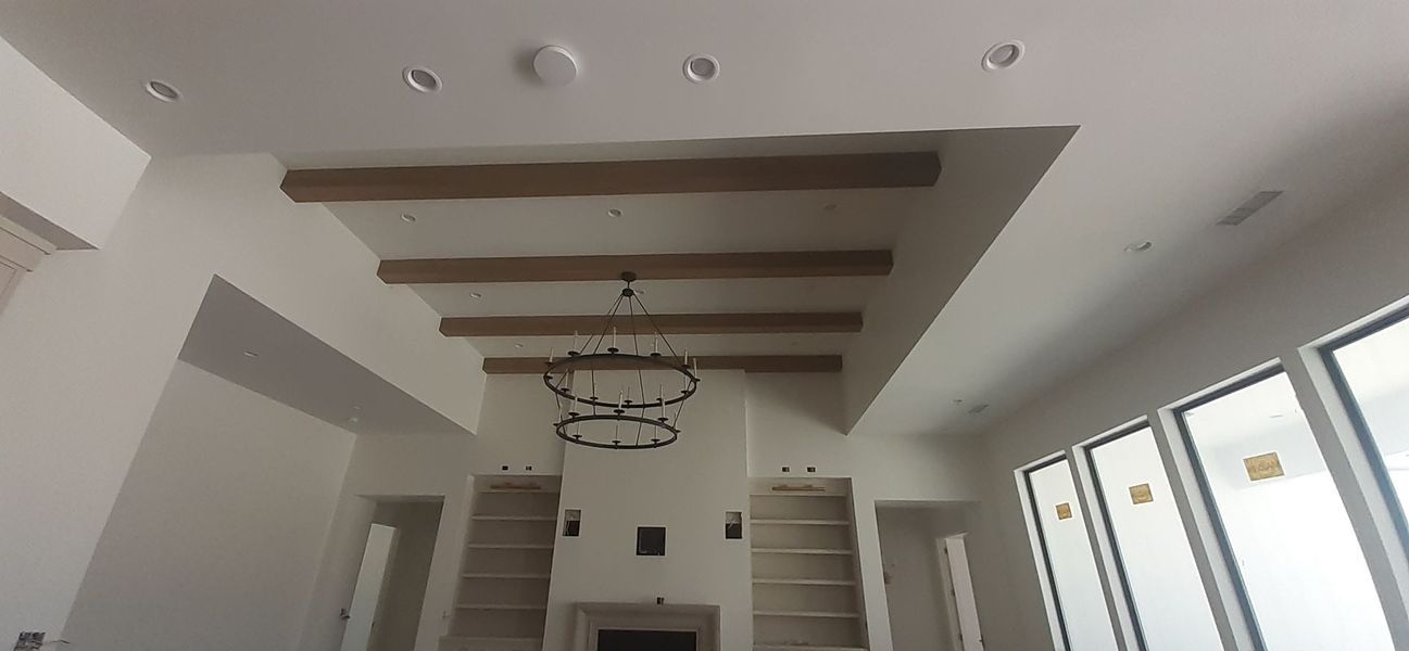 Interior of a white room with wooden beams on the ceiling, chandelier, and built-in shelves.