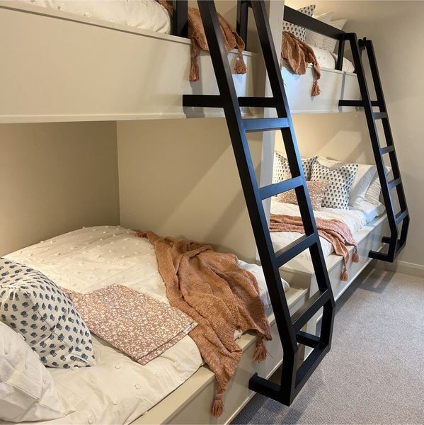 Two-tier bunk beds with black ladders and beige frame. Beds are made with white and pink blankets and pillows.
