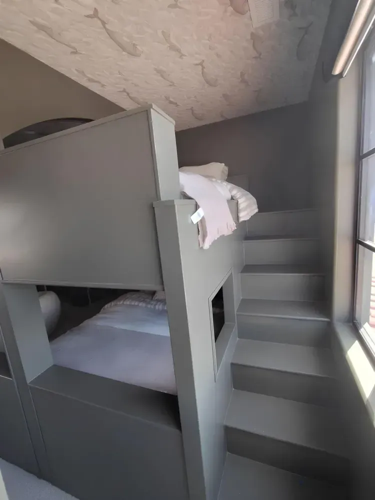 Gray bunk beds with steps, a window, and a patterned ceiling.