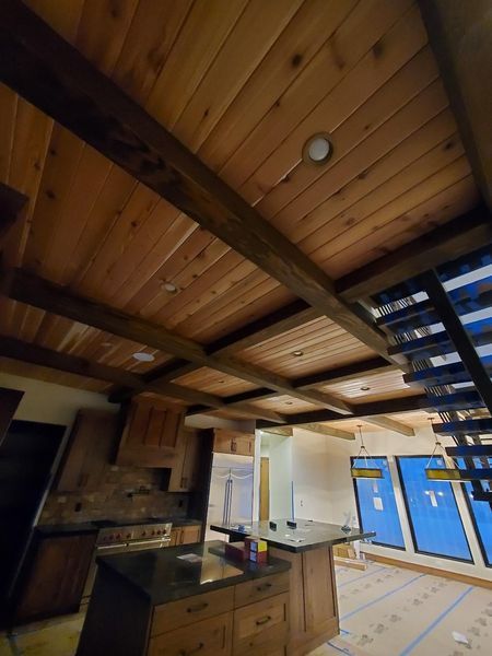 Wooden ceiling with dark beams in a home, featuring recessed lighting, a kitchen island, and a staircase.