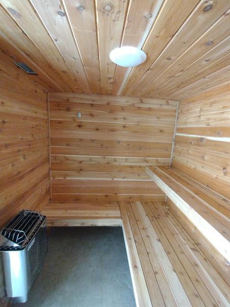 Interior of a cedar sauna with benches, a heater, and a ceiling light.