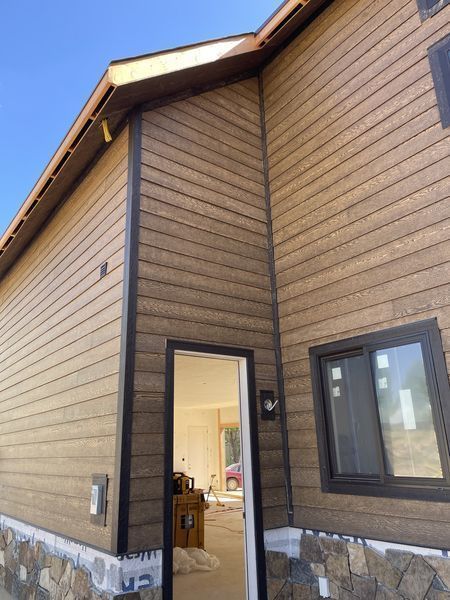 Brown-sided house exterior with dark trim and a stone base. Doorway and window visible.