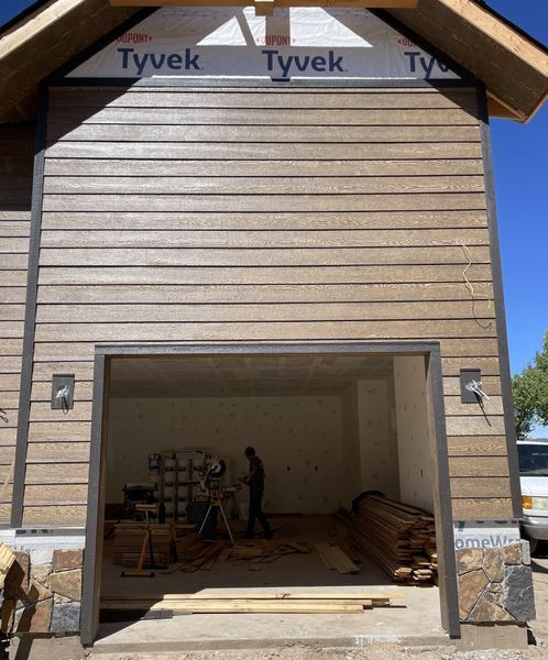 Garage under construction with brown siding, Tyvek wrap, stone accents, and a worker inside.