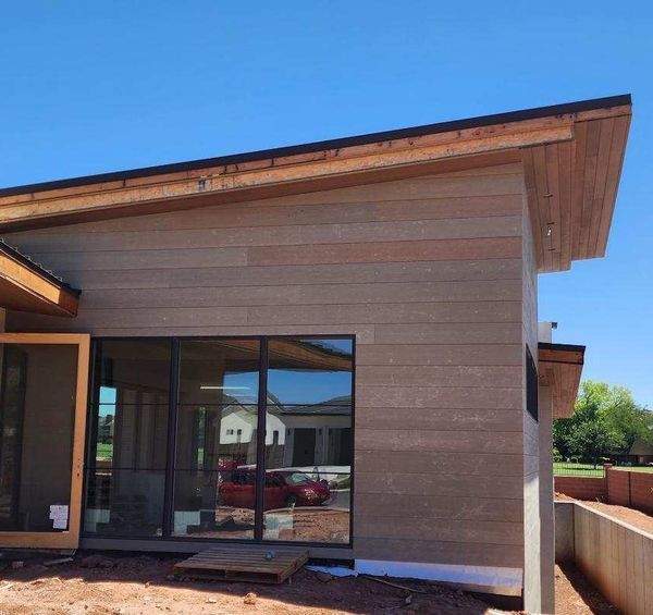 Modern house exterior with brown siding, large windows, and angled roof under blue sky.